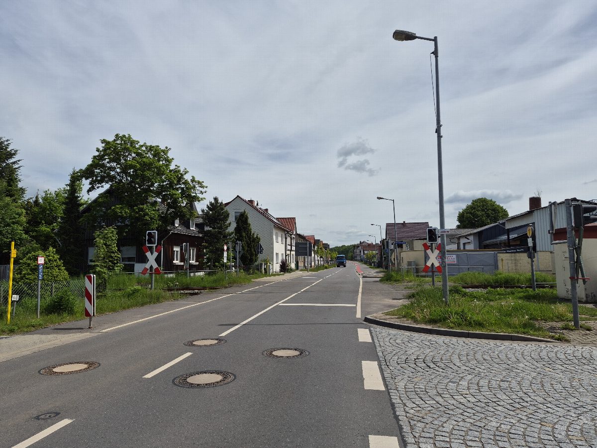 Neu ausgebaute Straße L1037 (Geschwister-Scholl-Straße) mit Schachtabdeckungen und Bahnübergang.
