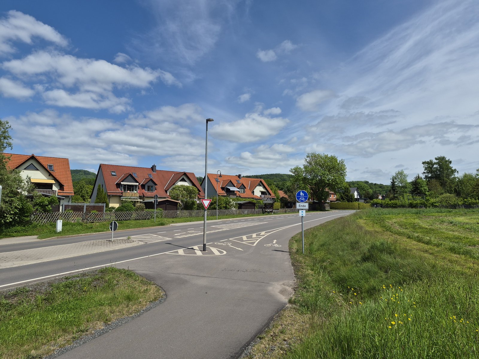 Radwegquerung an der L1037 mit Verkehrsinsel, Beschilderung und Wohnbebauung.